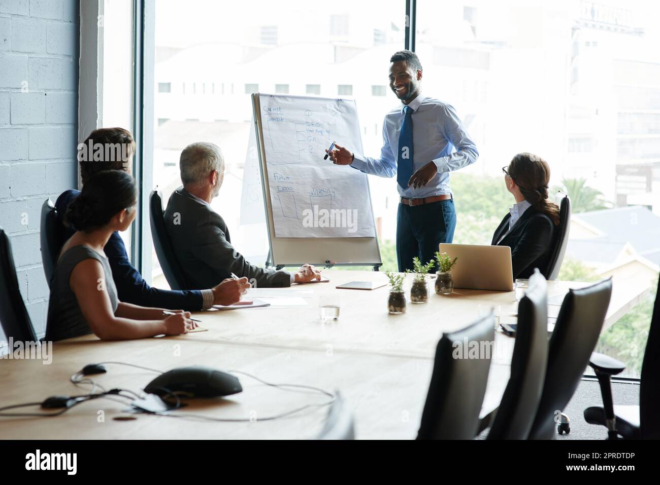 Junger schwarzer Mann hält Führungspräsentation über Innovation bei einer Aktionärsversammlung im Amt. Eine Gruppe unterschiedlicher Arbeitskollegen, die über die Unternehmensphilosophie und die Strategie zur Entwicklung der Vision spricht. Stockfoto