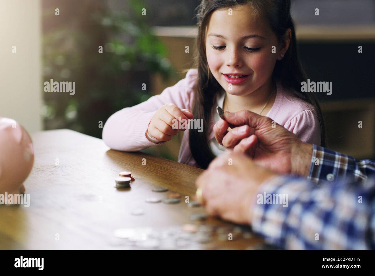 Je früher, desto besser. Ein kleines Mädchen, das von ihrem Großvater über Geld lernt. Stockfoto