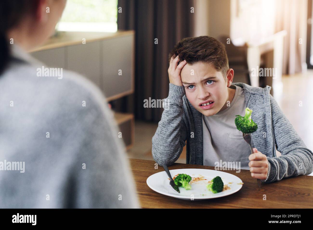 Wie kann alles, was schlecht schmeckt, gut für Sie sein? Eine Mutter sagt ihrem Sohn, er solle seinen Brokkoli essen, den er nicht mag. Stockfoto