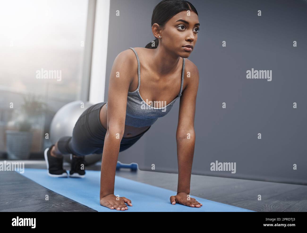 Unbeeindruckt von all dem stehen die Augen immer noch auf dem Preis. Eine attraktive junge Frau macht zu Hause Stretching-Übungen auf ihrer Fitnessmatte. Stockfoto