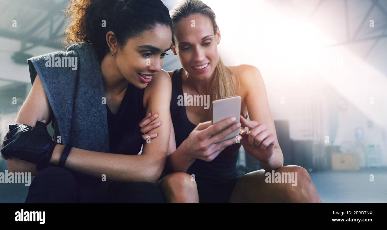 Zwei können das Spiel spielen. Zwei attraktive Sportlerinnen im Fitnessstudio sitzen und SMS lesen. Stockfoto