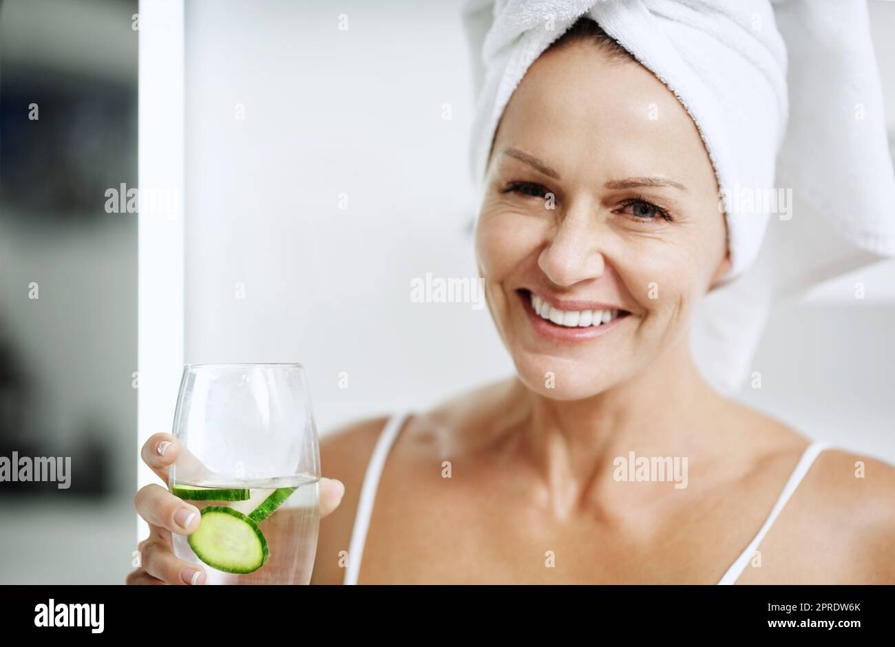 Probieren Sie es einfach aus, es funktioniert. Eine reife Frau hält ein Glas Wasser mit Gurke in sich. Stockfoto