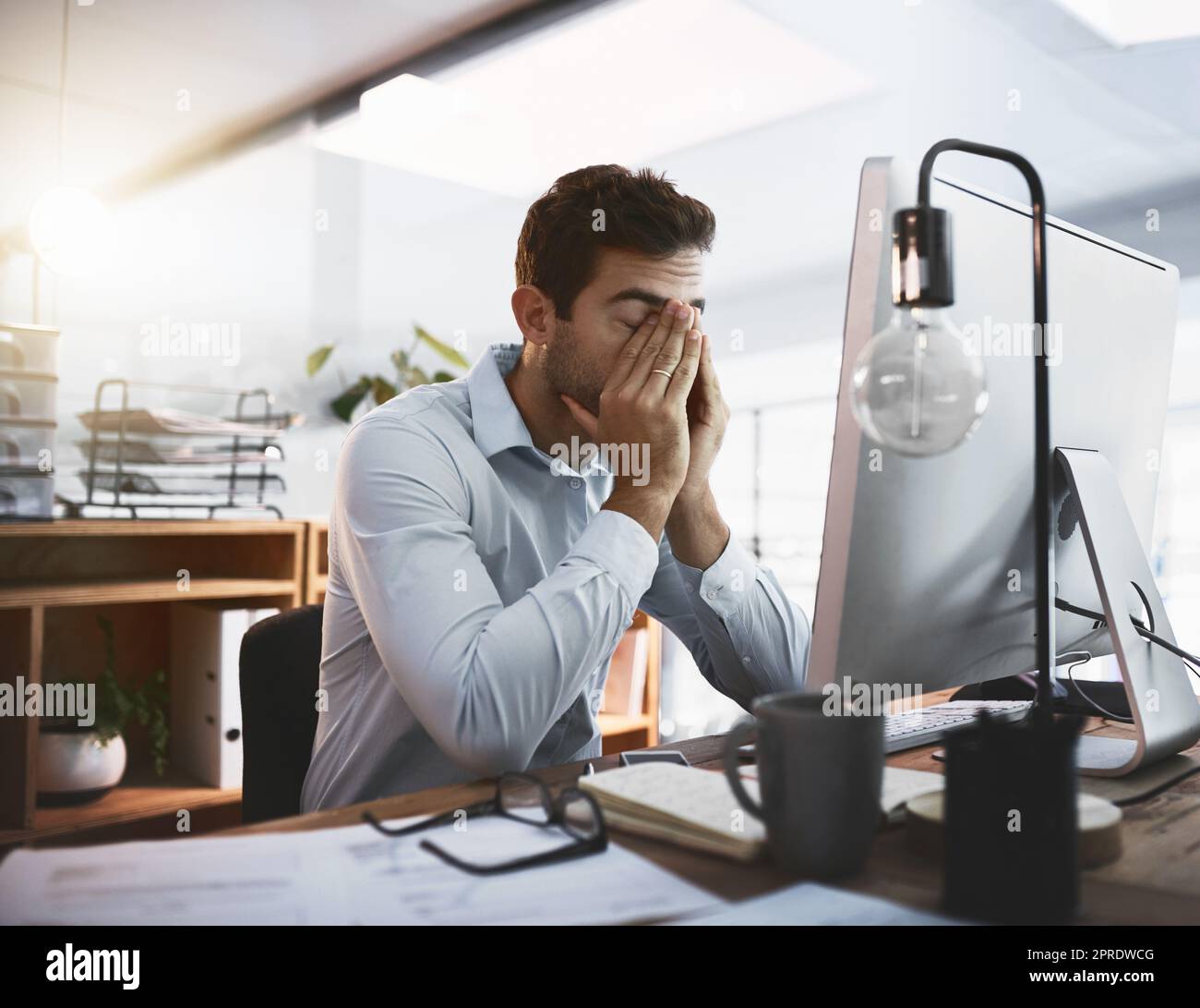 Die Anforderungen werden zu hoch. Ein junger Geschäftsmann, der gestresst schaut, während er spät am Computer in einem Büro arbeitet. Stockfoto