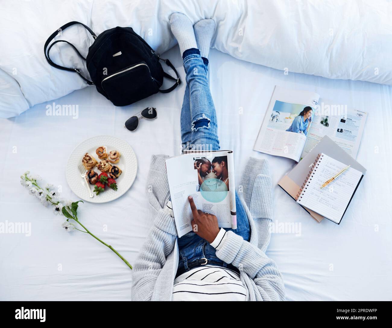 Bloggerin zu sein, ist ihr Hobby geworden. Aufnahmen aus dem Blickwinkel einer unbekannten Frau, die eine Zeitschrift liest und zu Hause auf ihrem Bett frühstückt. Stockfoto