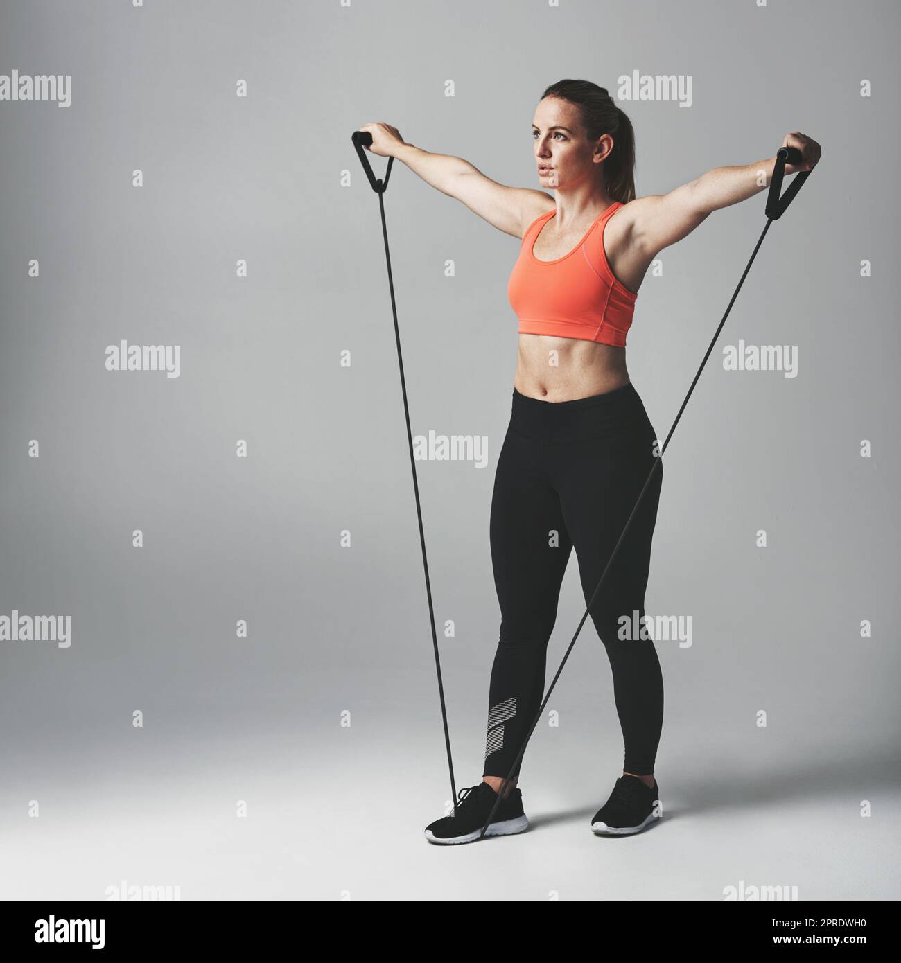 Krafttraining ist gut für den ganzen Körper. Studioaufnahme einer athletischen jungen Frau, die mit einem Widerstandsband vor grauem Hintergrund arbeitet. Stockfoto