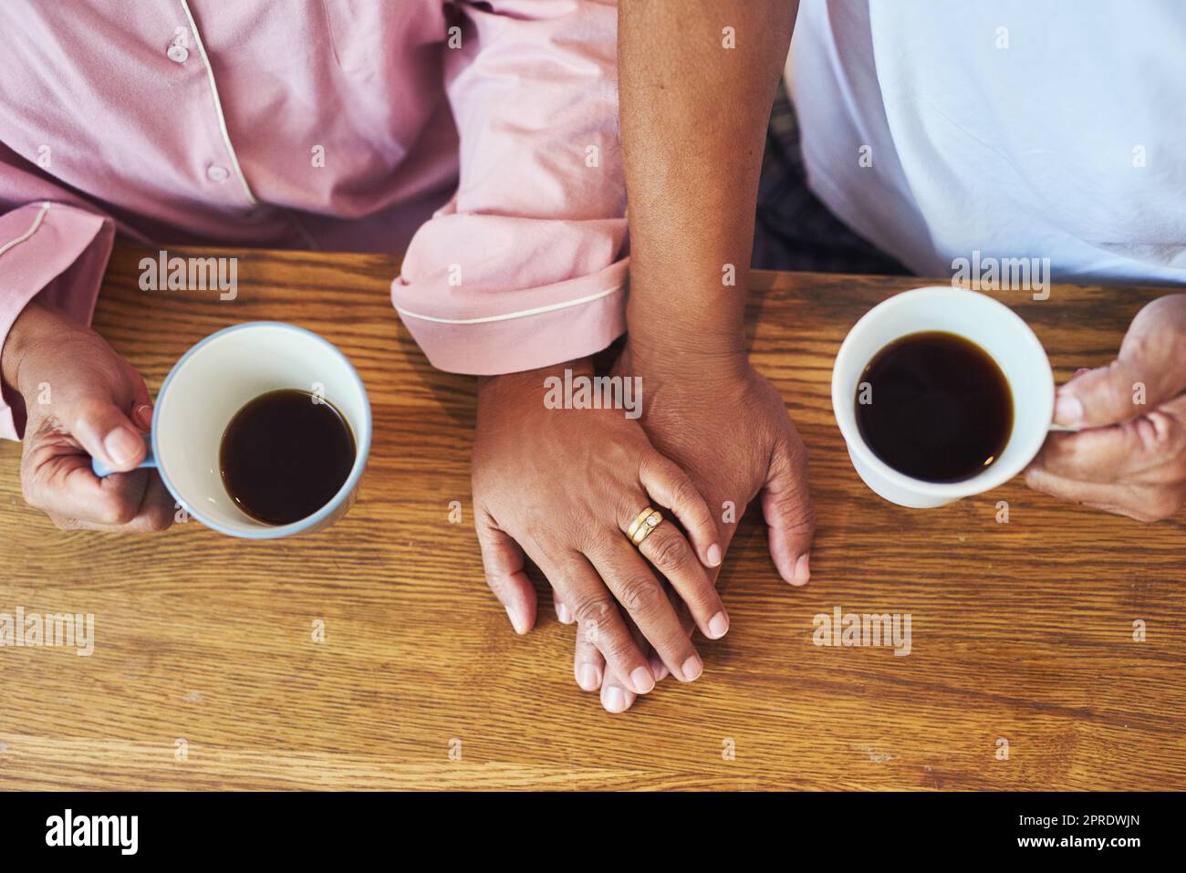 Wir genießen die einfachen Dinge im Leben. Nahaufnahme eines nicht wiedererkennbaren Paares, das sich an den Händen hält, während er tagsüber Kaffee auf einem Tisch zu Hause trinkt. Stockfoto