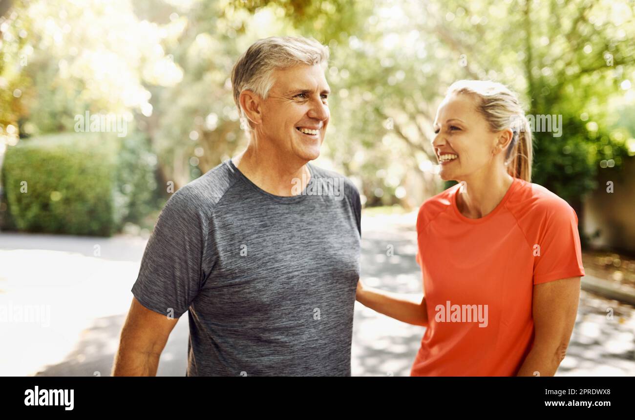 Glückliches, reifes Paar, das aktiv, fit und gesund bleibt, während es in der Natur joggt, joggt oder spaziert. Lachender älterer Mann und lachende Frau, die eine Pause vom Training oder Training genießen Stockfoto