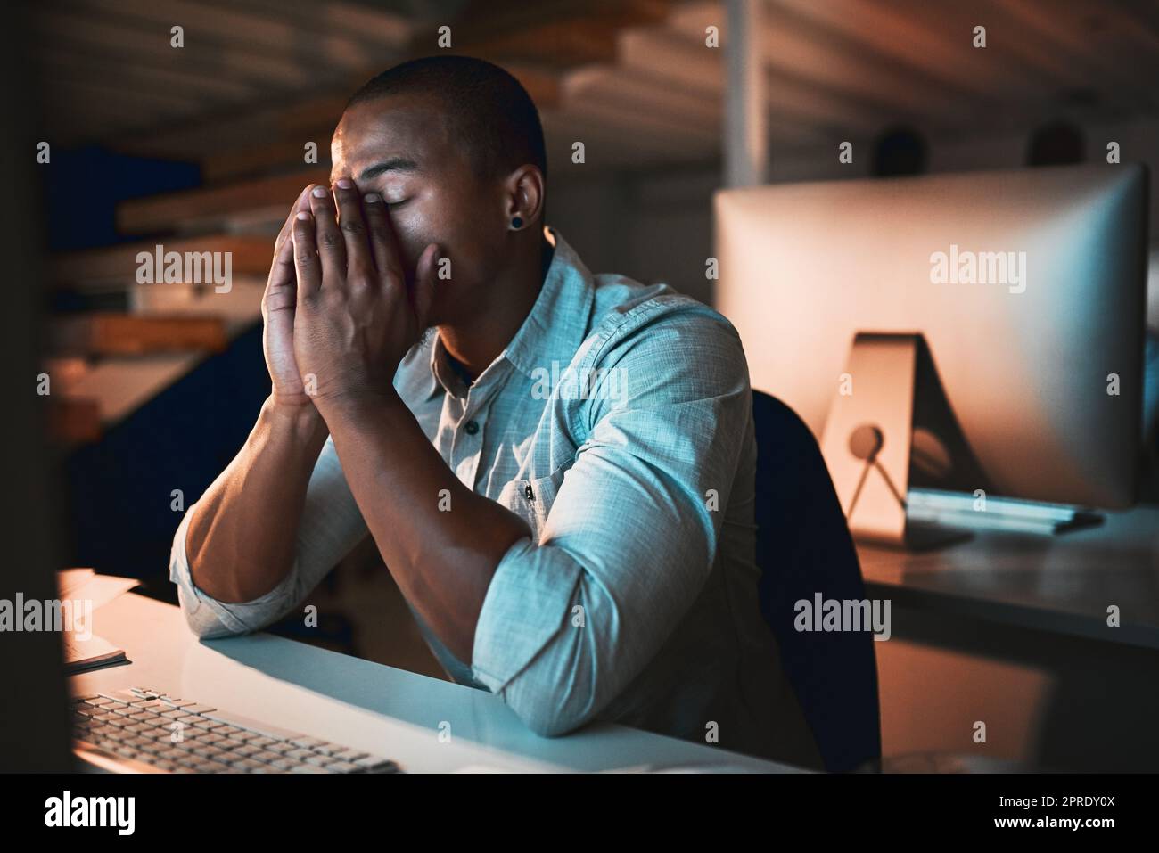 Ein junger männlicher Designer, der gestresst aussieht, während er im Büro an seinem Computer arbeitet. Stockfoto