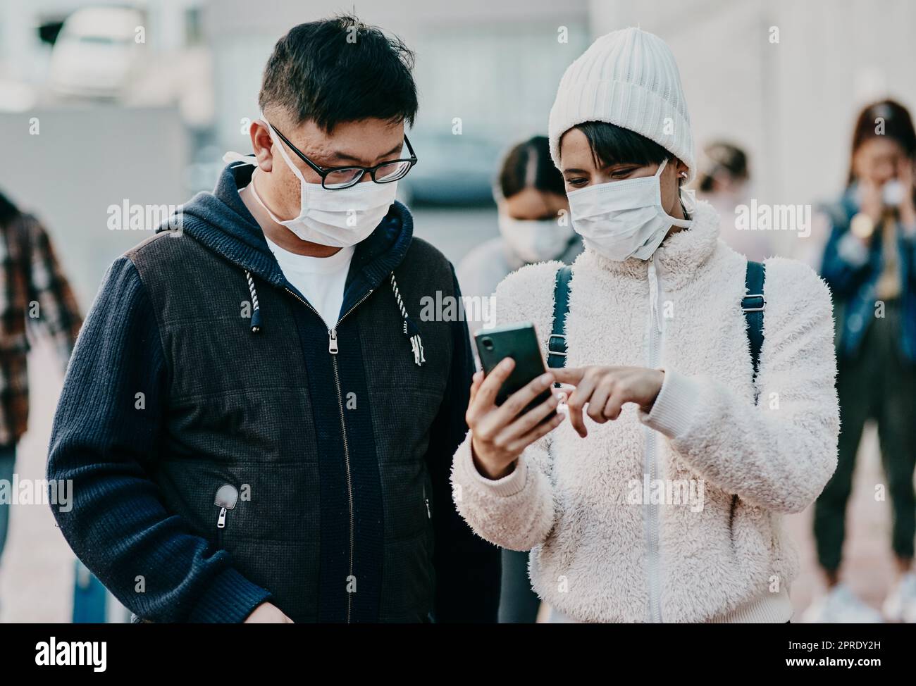 Menschen mit koviden Gesichtsmasken und Telefonen suchen online nach Informationen, die sich die Nachrichten über Reiseverbote in sozialen Medien ansehen, während sie an der Grenze gestrandet sind. Moderne ausländische Reisende am Flughafen Stockfoto