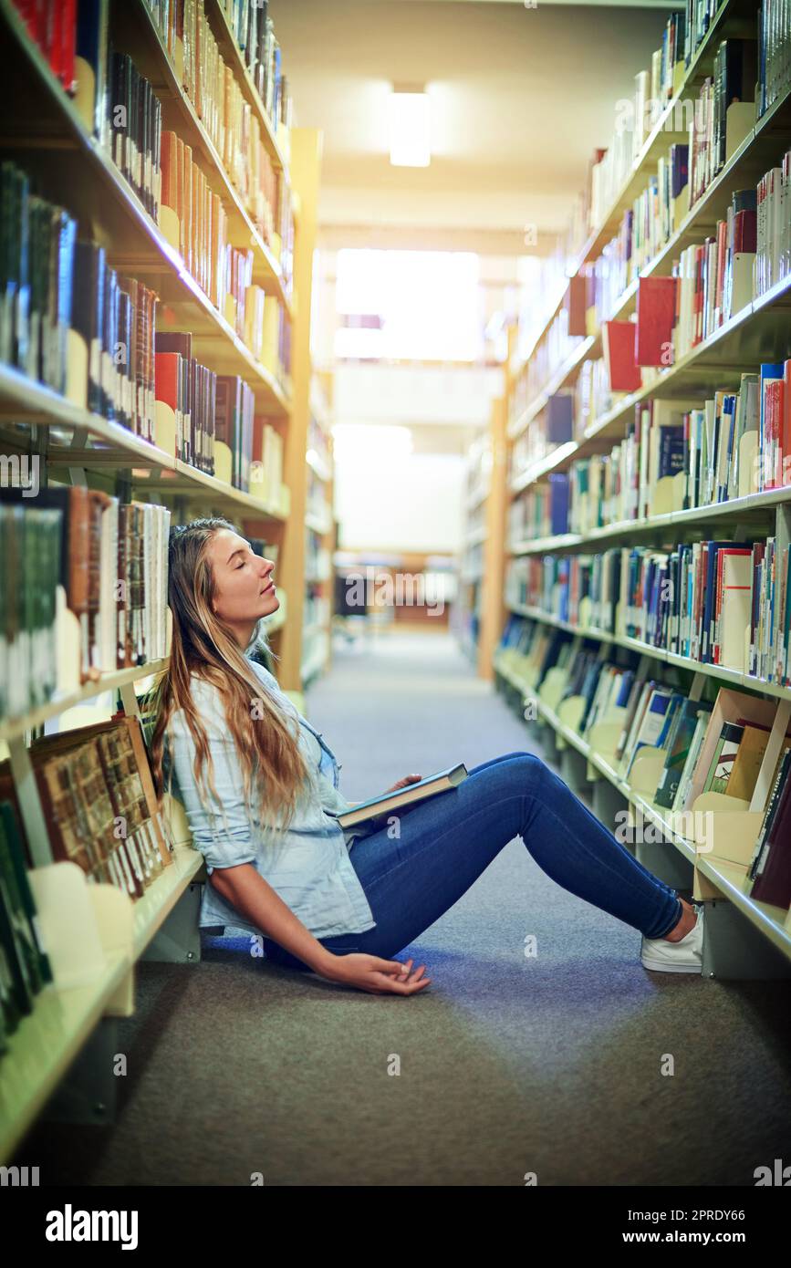 Das Leben im College kann manchmal ziemlich ermüdend sein. Ein Universitätsstudent schläft zwischen den Bücherregalen in der Bibliothek auf dem Campus. Stockfoto
