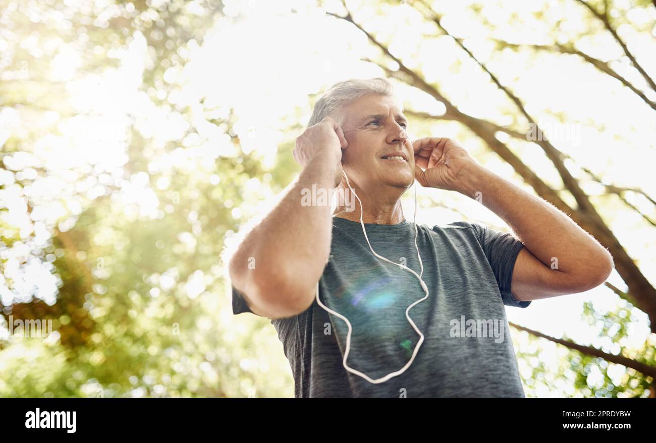 Gesunder, fitter und aktiver Senior man hört Musik beim Laufen, Training und Training draußen von unten. Fröhlicher, sportlicher und wirklich reifer Mann, der ein Kardio- und Ausdauertraining im Freien macht Stockfoto