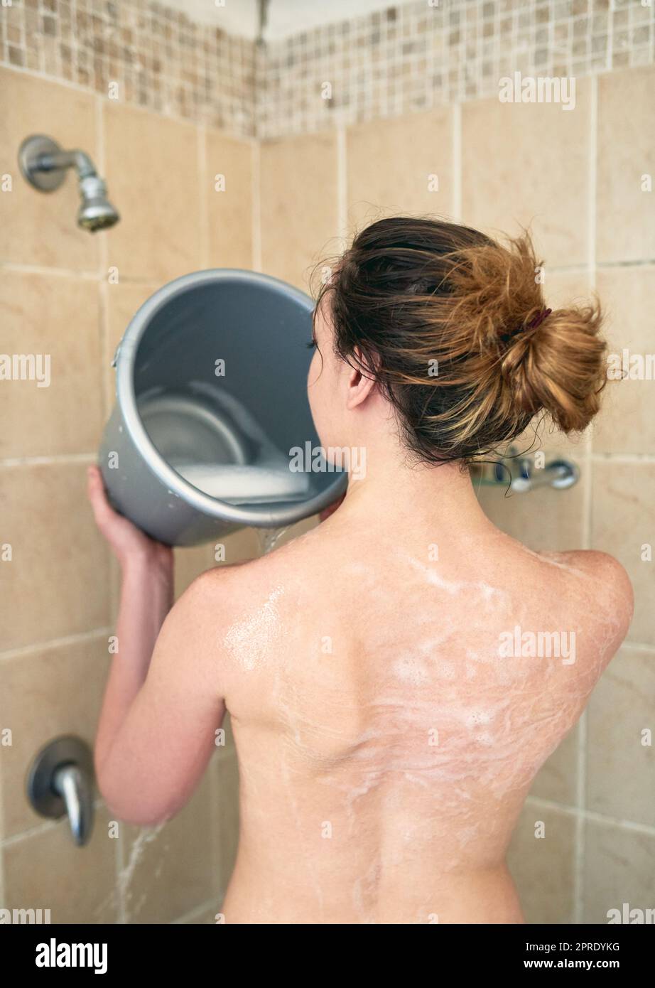 Wasser sparen, Geld sparen und den Planeten retten. Rückansicht einer unkenntlichen Frau, die ihren Körper mit einem Eimer Wasser im Badezimmer zu Hause wäscht. Stockfoto