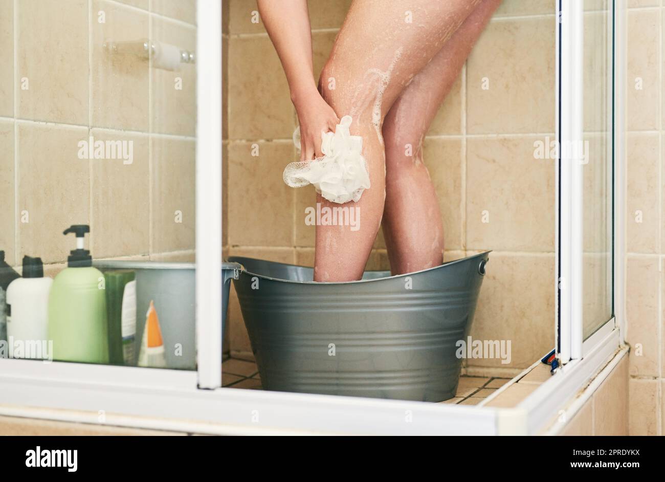 Es gibt einfache Möglichkeiten, Wasser zu sparen. Eine unkenntliche Frau wäscht in einem Eimer, der zu Hause in die Dusche gestellt wurde. Stockfoto
