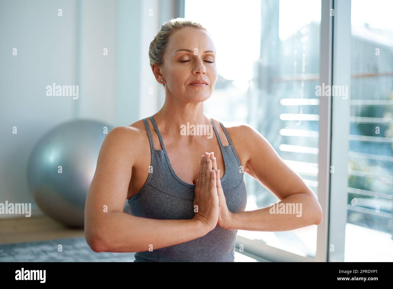 In perfekter Balance. Eine attraktive reife Frau, die zu Hause meditiert. Stockfoto