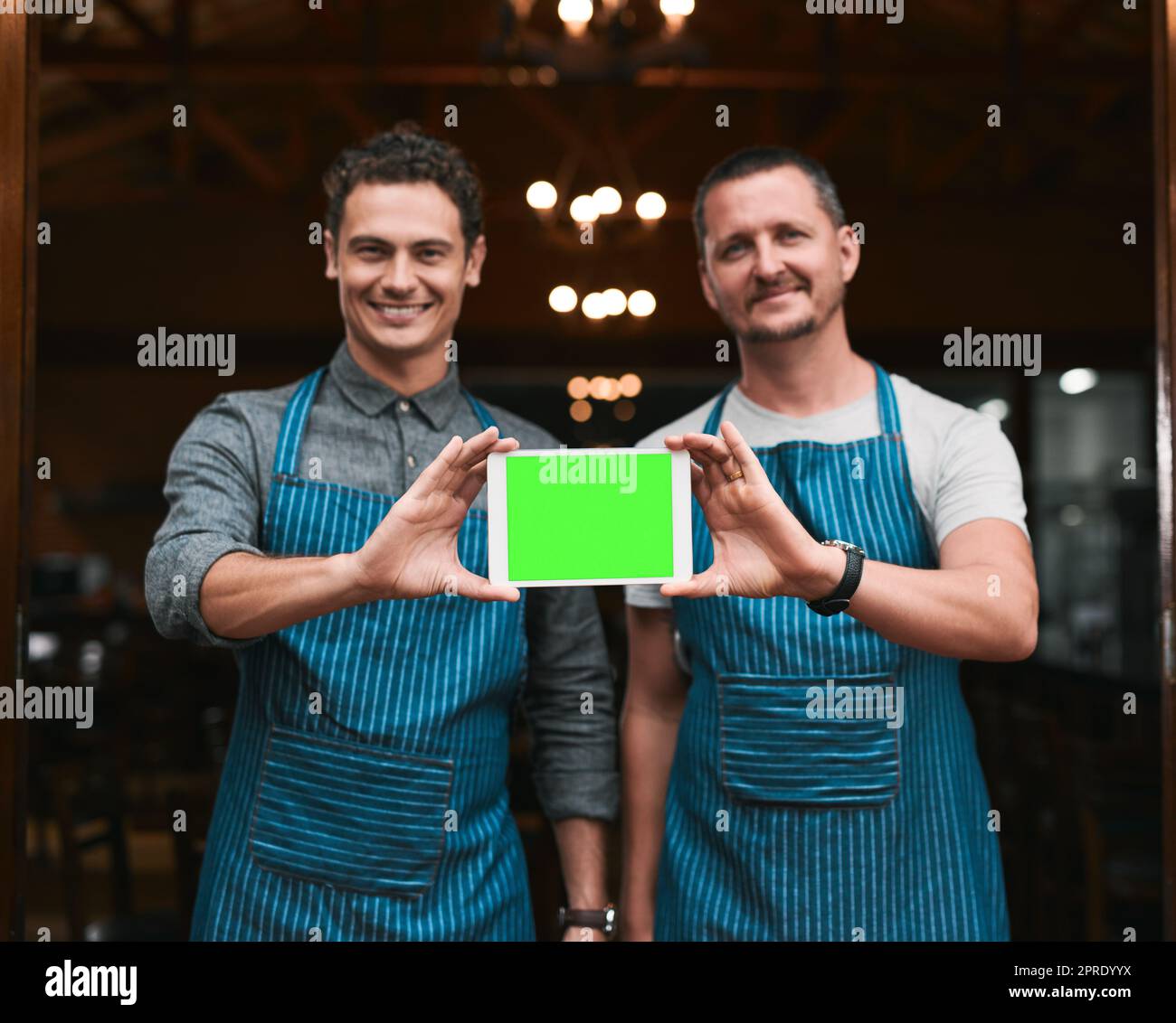 Willkommen in unserem Geschäft. Porträt von zwei fröhlichen Geschäftsleuten, die ein digitales Tablet zusammenhalten, während sie vor den Türen einer Bierbrauerei stehen. Stockfoto