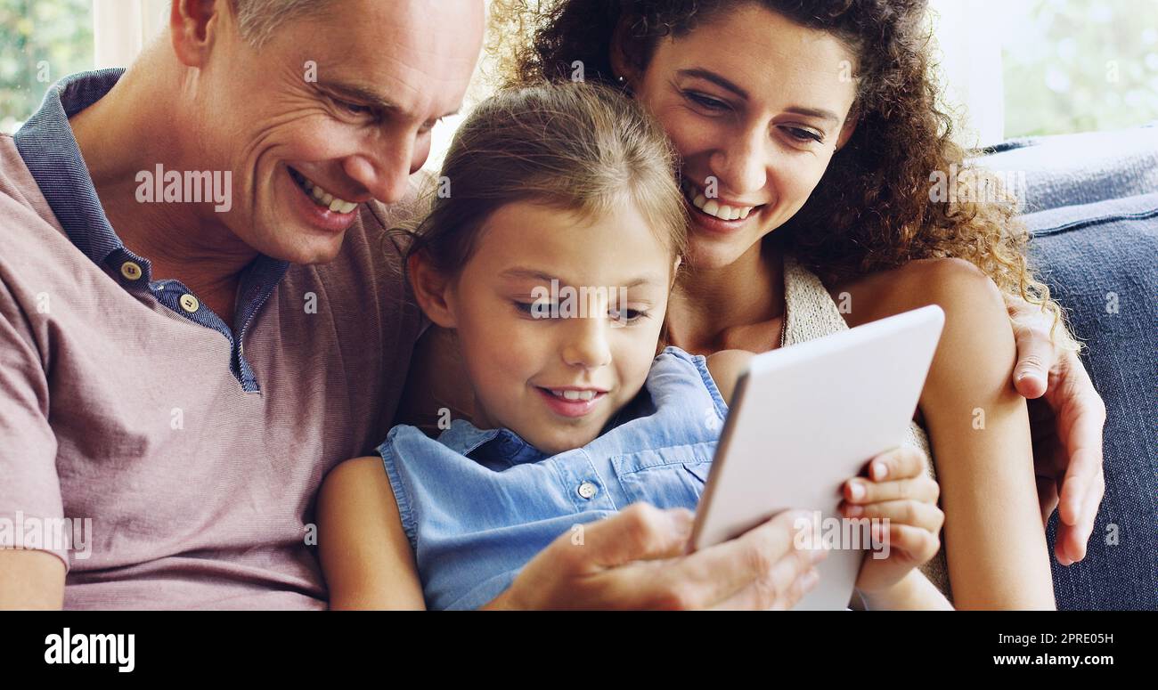Familienzeit im digitalen Zeitalter. Ein süßes kleines Mädchen, das mit Mutter und Vater ein digitales Tablet zu Hause auf dem Sofa benutzt. Stockfoto