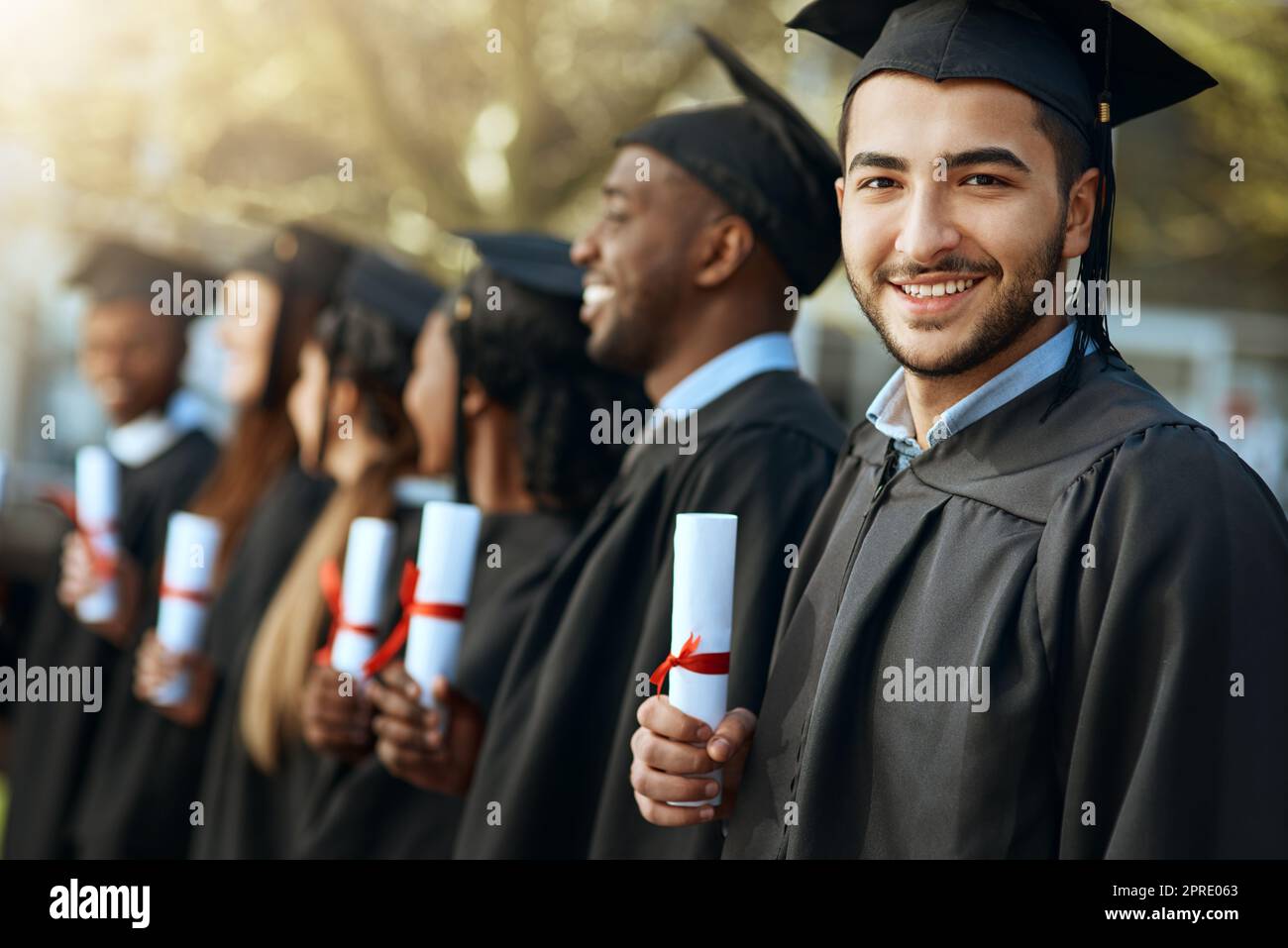 Stolz beginnt nicht, das Gefühl zu beschreiben. Porträt eines jungen Mannes, der sein Diplom hält, während er mit seinen Mitstudenten am Abschlusstag steht. Stockfoto