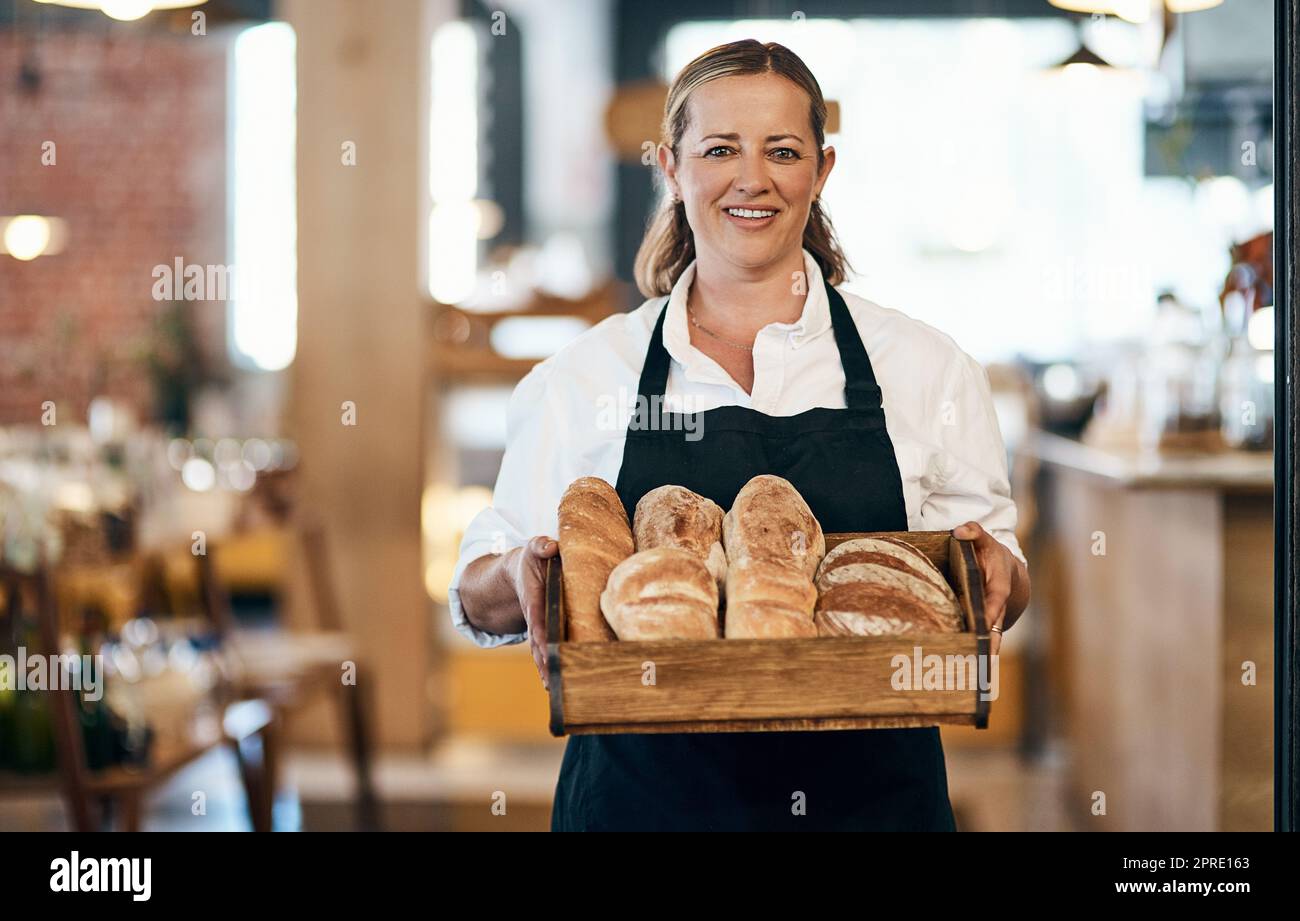 Baker, Café-Besitzer und Konditor, der in einem kleinen Café als Unternehmer und Jungunternehmer arbeitet. Porträt einer Köchin in einer Schürze, die eine Packung Brötchen in ihrer Bäckerei trägt Stockfoto