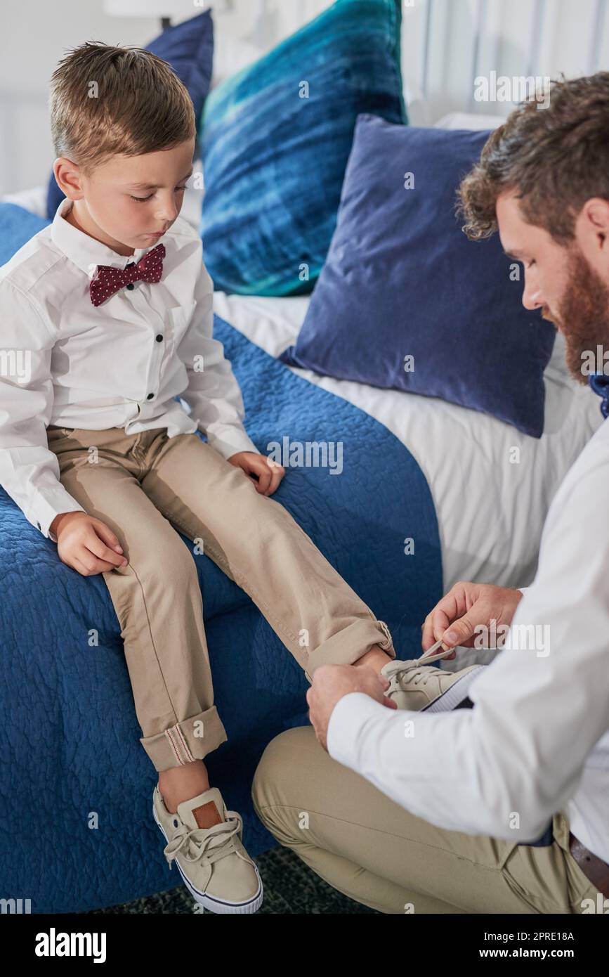 Daddys lehrt mich, wie ich meine Schnürsenkel binden kann. Ein junger, hübscher Vater bindet seine Söhne zu Hause Schnürsenkel. Stockfoto