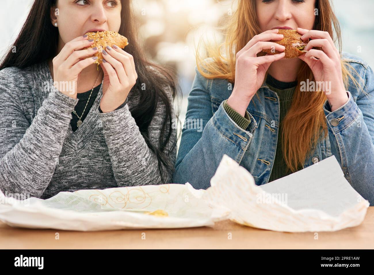 Zwei weibliche beste Freunde essen Sandwiches in einem Vergnügungspark draußen. Stockfoto