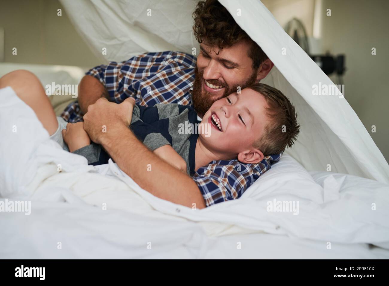 Hier kommt das Kitzelmonster. Ein hübscher junger Mann und sein Sohn spielen zu Hause auf dem Bett. Stockfoto