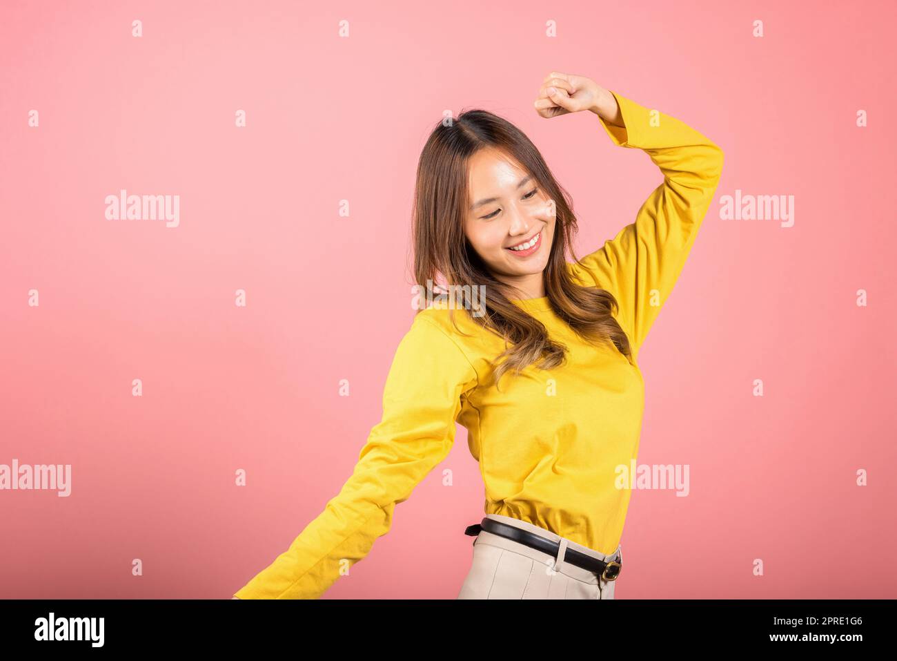 Asiatische junge Frau tanzt mit inspiriertem Gesichtsausdruck und hebt die Hände hoch Stockfoto