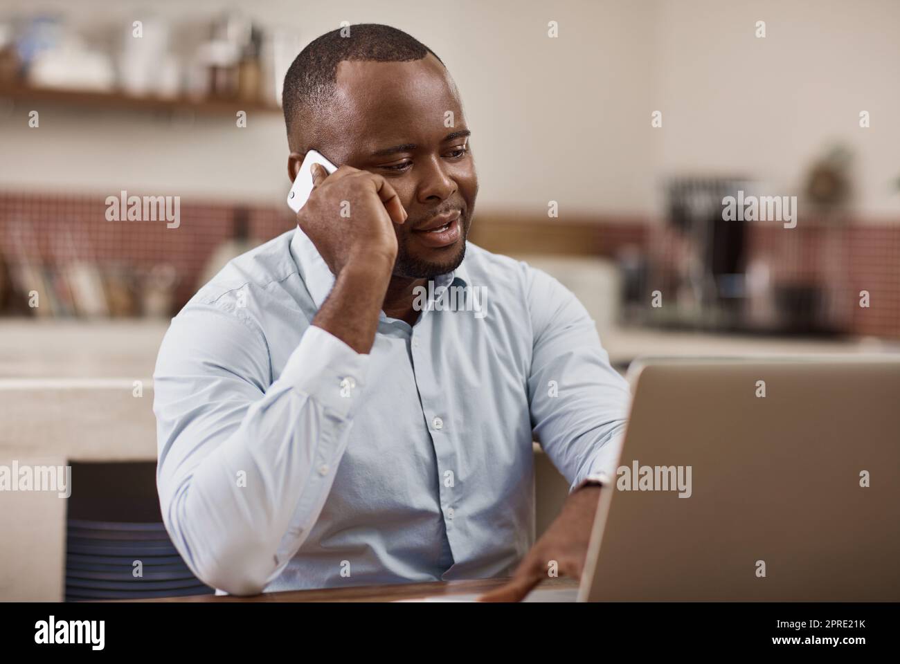 Gib mir einfach eine Zeit und einen Platz. Ein hübscher junger Geschäftsmann, der zu Hause an seinem Laptop arbeitet und einen Telefonanruf abgibt. Stockfoto