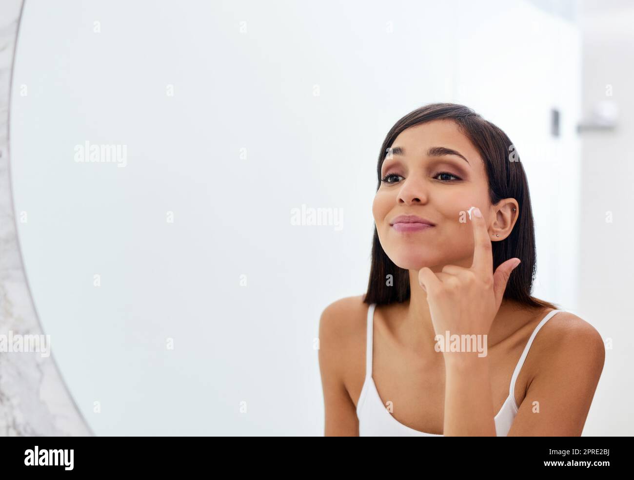 Halten Sie sich an eine Routine, die am besten für Sie funktioniert. Eine attraktive junge Frau Anwendung Feuchtigkeitscreme auf ihr Gesicht im Badezimmer. Stockfoto