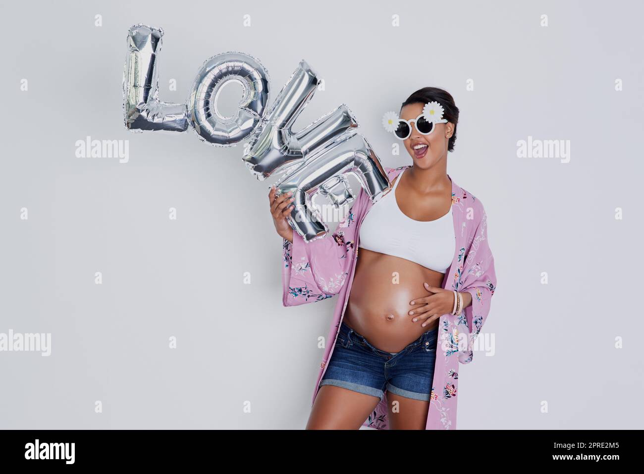 Keine große Liebe wie eine Mutter für ihr Baby. Studioaufnahme einer schönen, jungen schwangeren Frau, die ein Wort mit einem Ballon hält, das Liebe vor grauem Hintergrund liest. Stockfoto