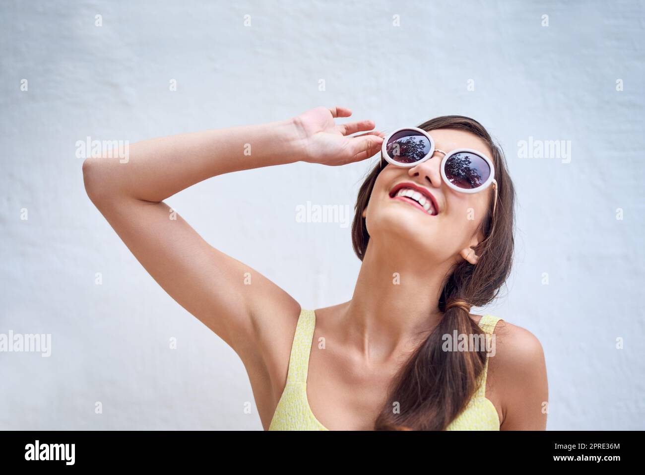 Bringen Sie die Sonne auf. Studioaufnahme einer fröhlichen jungen Frau, die eine Sonnenbrille trägt und vor einem grauen Hintergrund posiert. Stockfoto