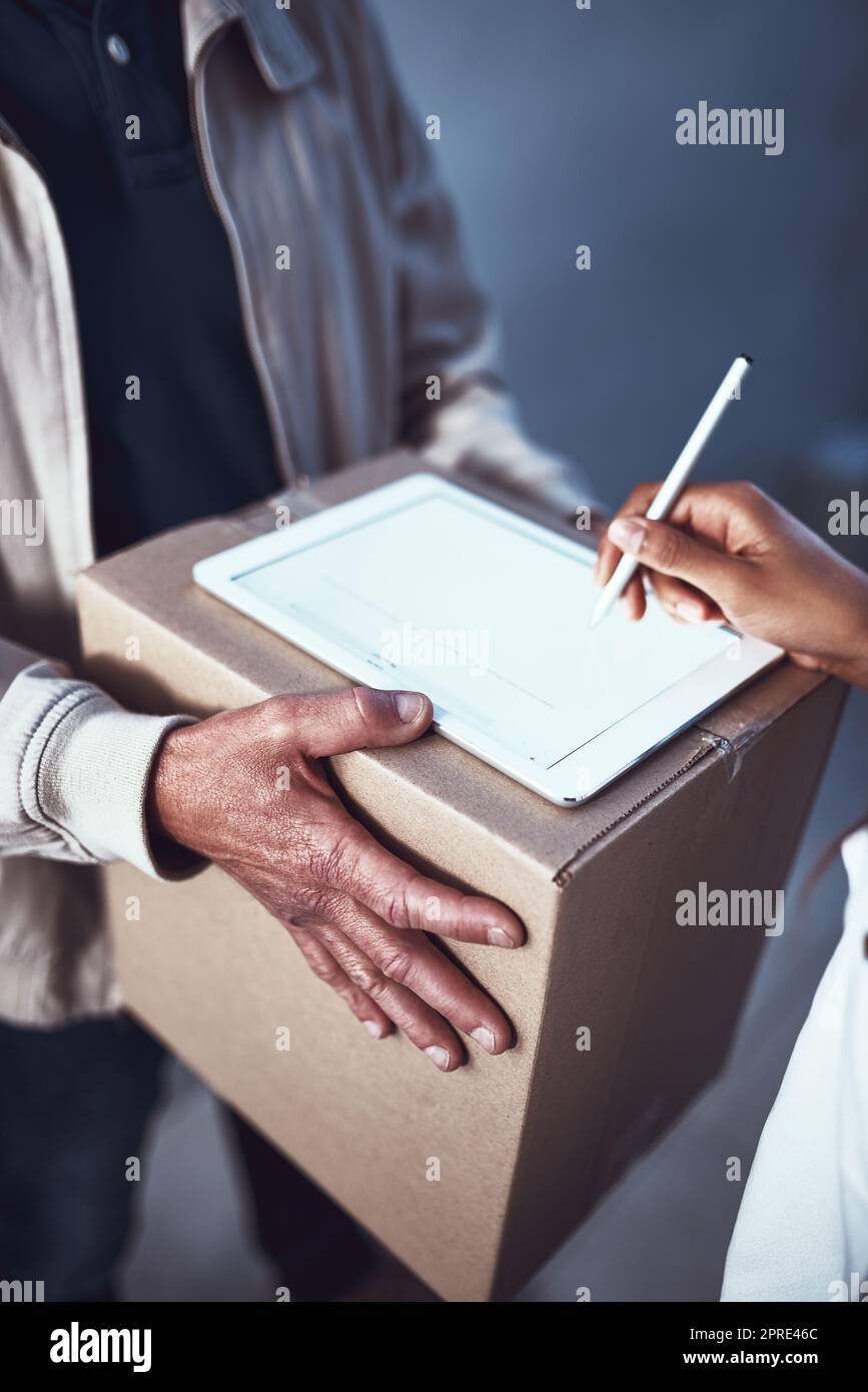 Ihr Paket ist sicher und gesund. Ein unkennbarer Mann übergibt einem Kunden ein Paket und lässt ihn auf einem digitalen Tablet unterschreiben. Stockfoto