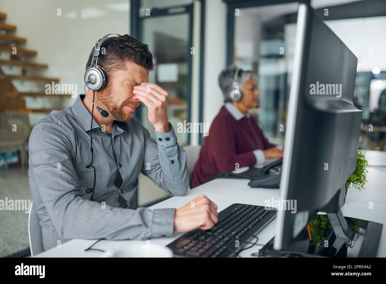 Der Tag hat einige Spannungen mit sich gebracht. Ein reifer Mann, der gestresst aussicht, während er an einem Computer in einem Callcenter arbeitet. Stockfoto