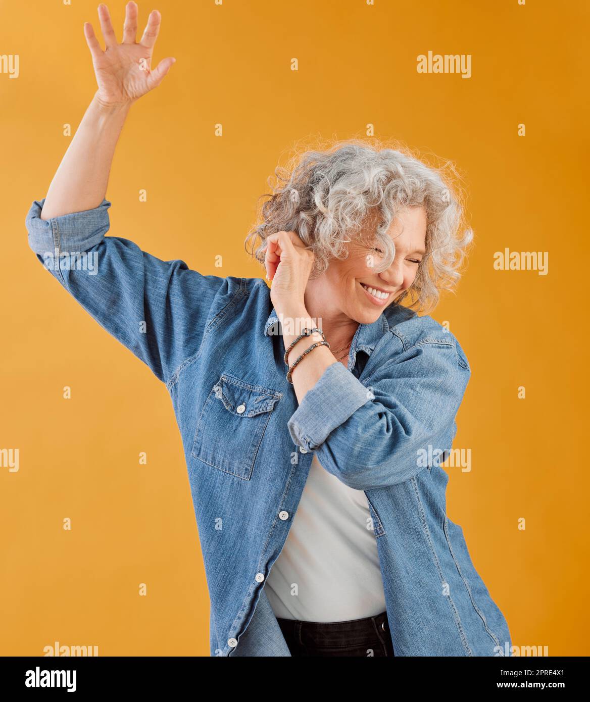 Feier, Feier und Tanz reife Frau, glückliche und fröhliche Senior, winkende Hand-Geste und Lächeln. Ältere weiße Frau, die Spaß hat, während sie vor orangefarbenem Hintergrund tanzt Stockfoto