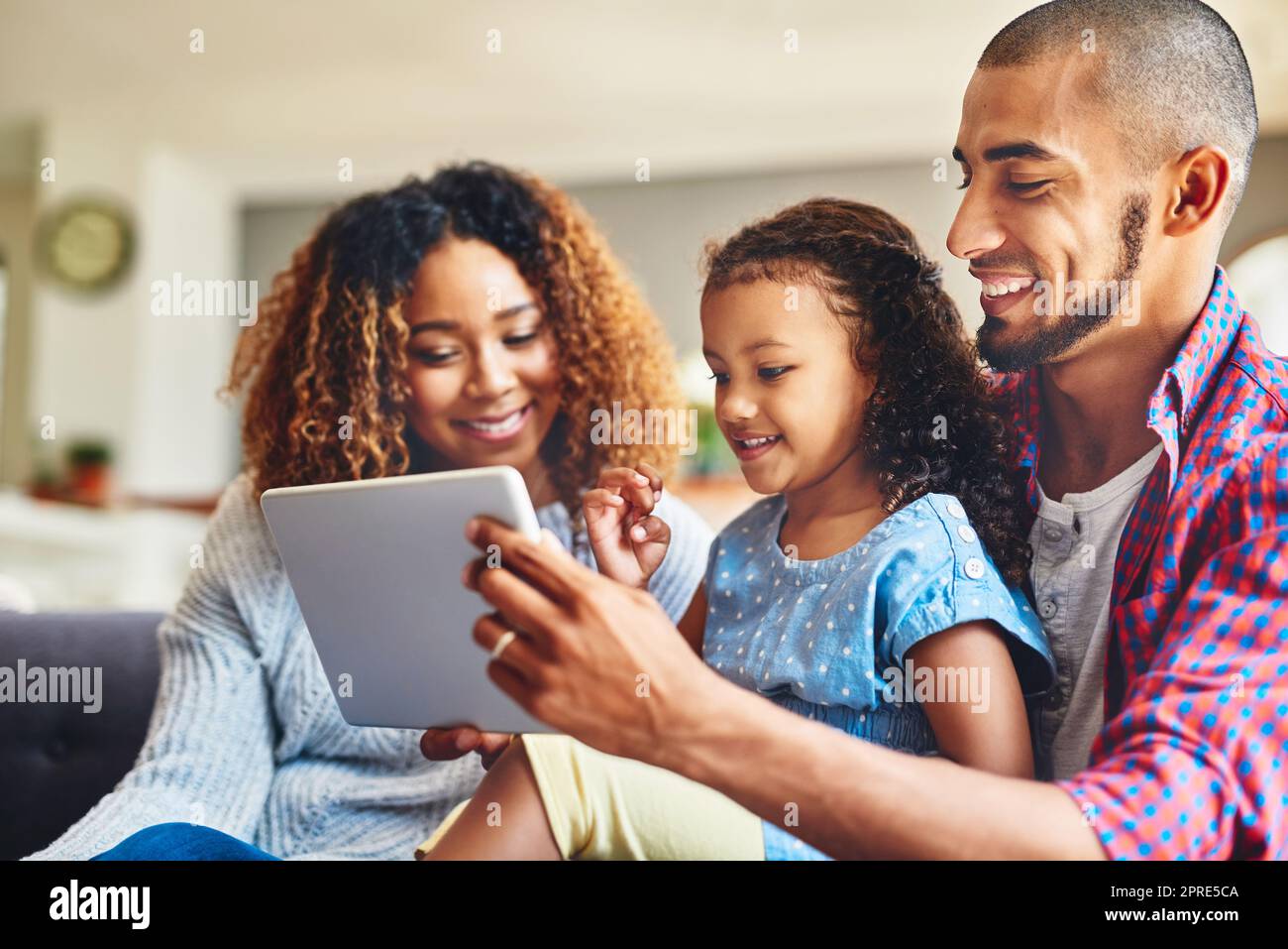 Zeit für das Lernen in der Familie. Ein entzückendes kleines Mädchen und ihre Eltern nutzen zu Hause ein digitales Tablet zusammen auf dem Sofa. Stockfoto