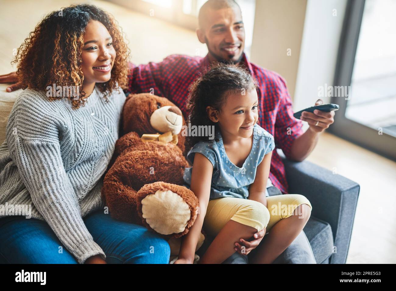 Die Elternschaft wählt familienfreundliche Filme für einen Sonntagnachmittag. Eine glückliche junge Familie von drei Kindern schaut zu Hause vom Sofa aus fern. Stockfoto