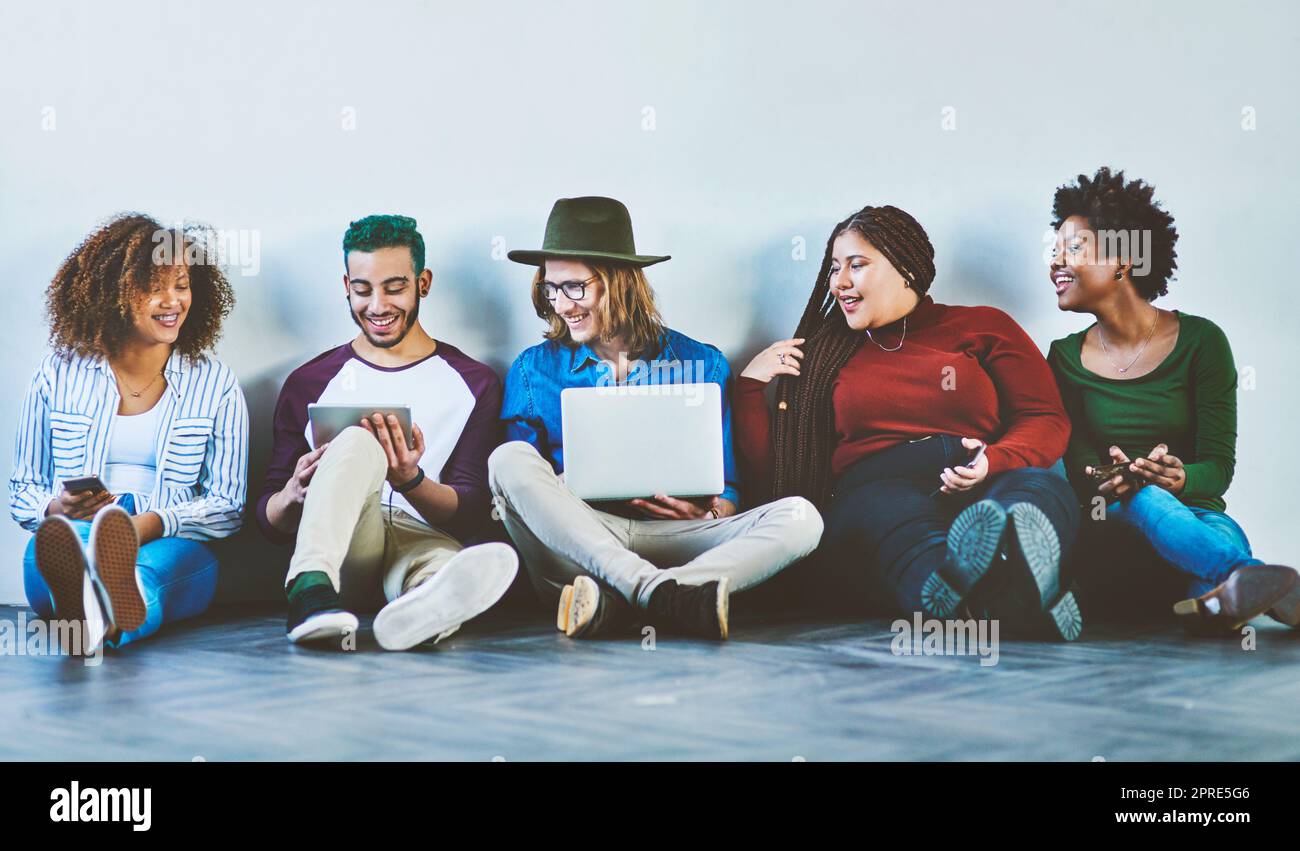 Es ist eine kabellose Welt, in der wir lebten. Studioaufnahme einer Gruppe junger Menschen, die auf dem Boden sitzen und drahtlose Technologie verwenden. Stockfoto