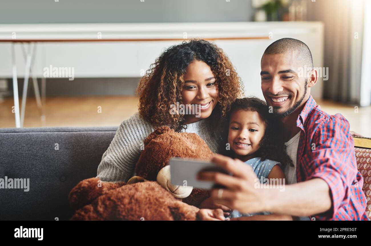 Familienzeit ist die beste Zeit für ein Selfie. Ein entzückendes kleines Mädchen, das mit ihren Eltern zu Hause auf einem Handy Selfies macht. Stockfoto