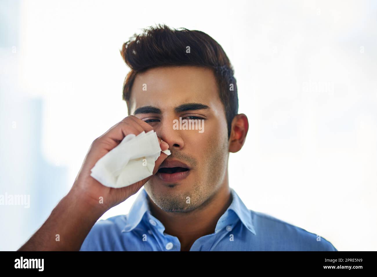 Ich muss nach Hause kommen und mich ausruhen. Ein junger Geschäftsmann bläst sich bei der Arbeit die Nase. Stockfoto