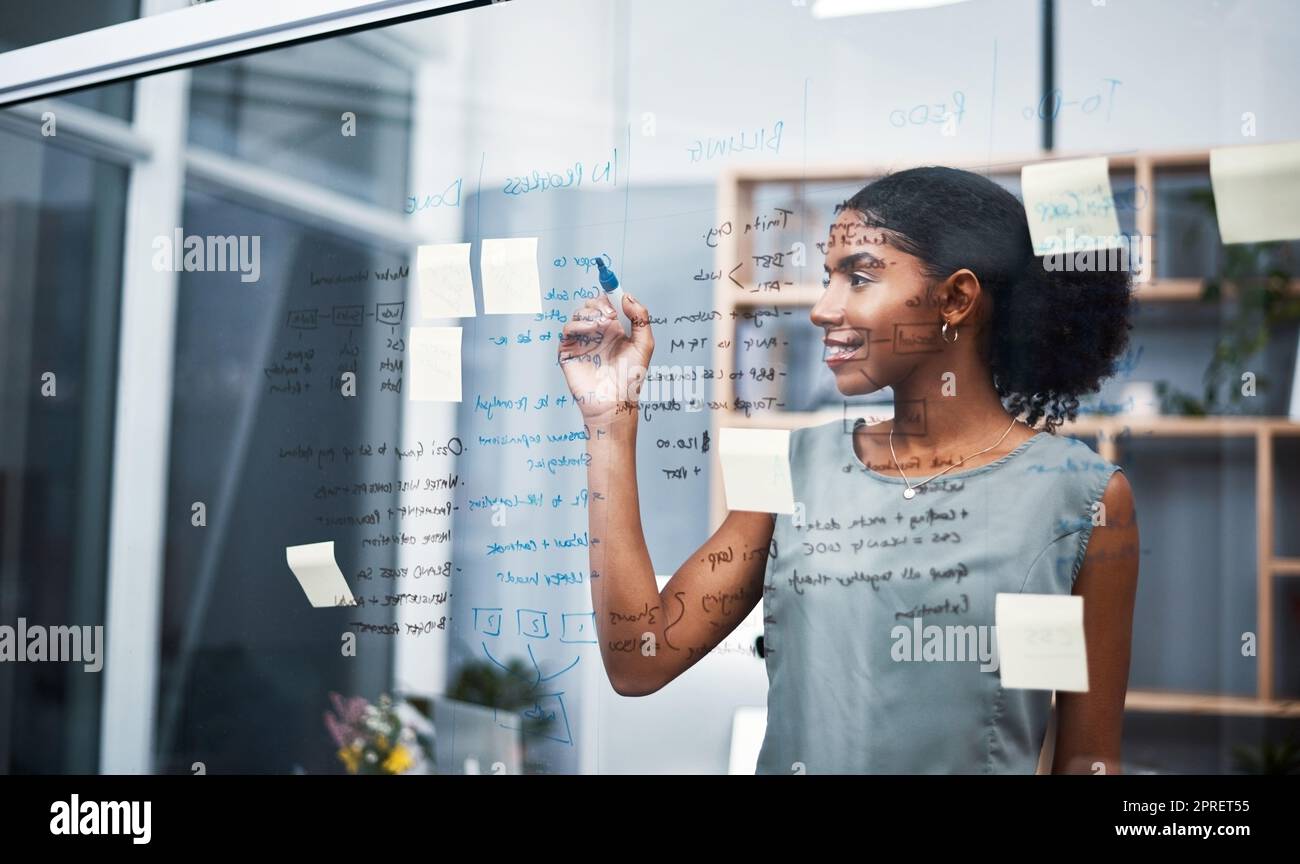 Weibliche Führungskräfte und Marketing-Profis sammeln Ideen für Innovationen, schreiben auf transparente Tafel mit Haftnotizen im Büro. Jungunternehmer, die den Auftrag und die Strategie des Unternehmens planen. Stockfoto