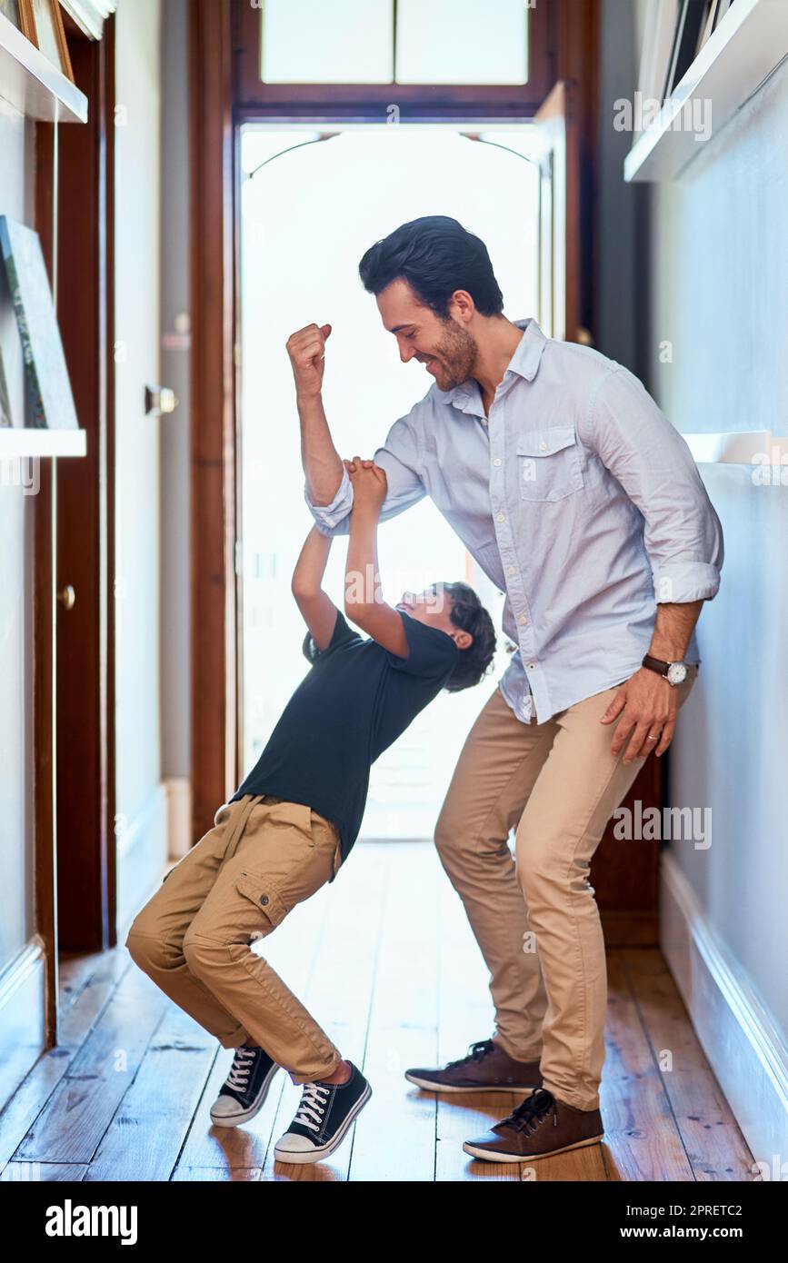 Wie stark bist du Vater. Ein fröhlicher junger Mann hebt seinen kleinen Jungen, der tagsüber zu Hause am Arm hängt. Stockfoto