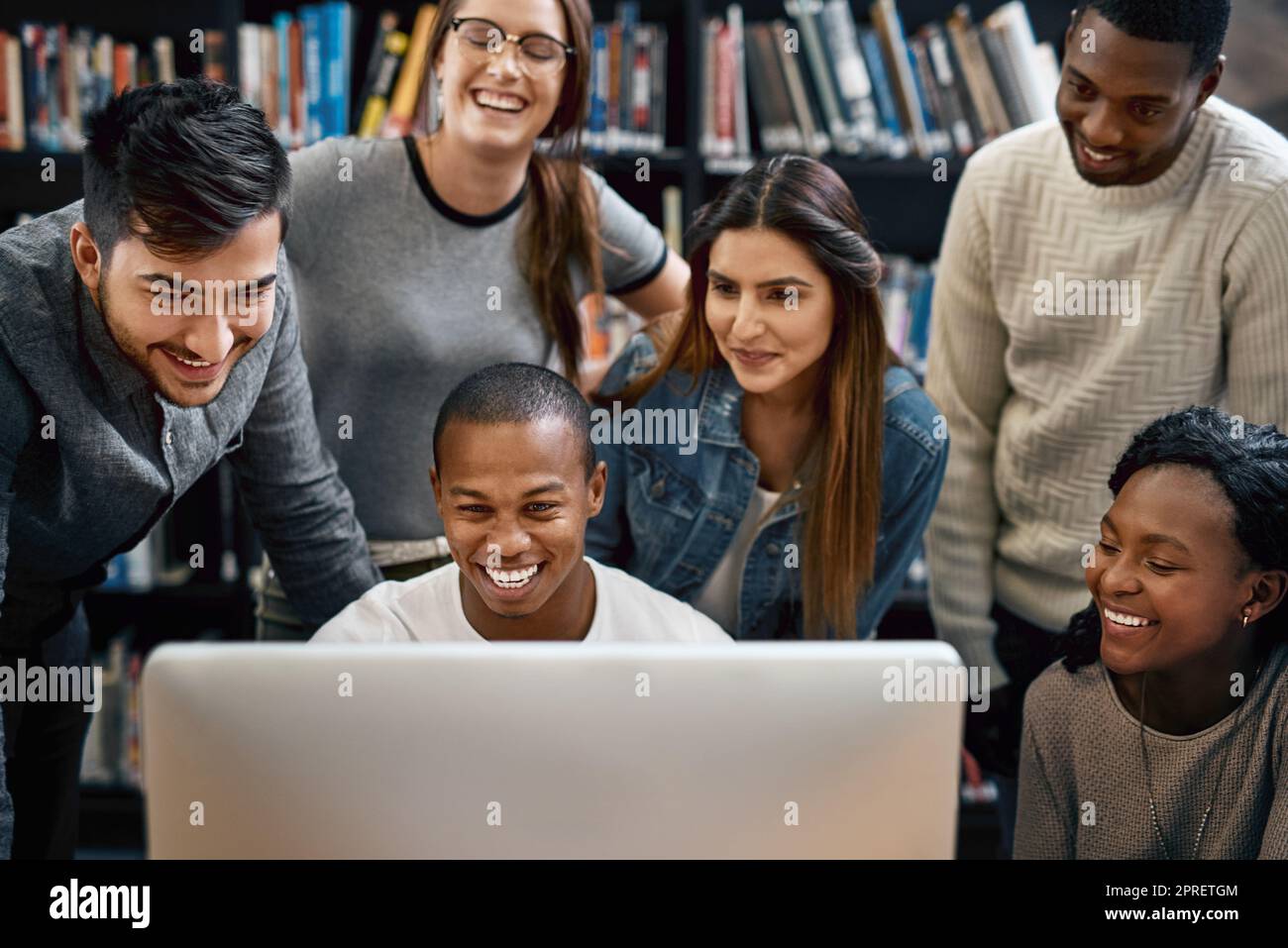 Umgeben Sie sich mit akademisch gesinnten Menschen. Eine Gruppe junger Studenten, die einen Computer zusammen in einer Universitätsbibliothek benutzen. Stockfoto