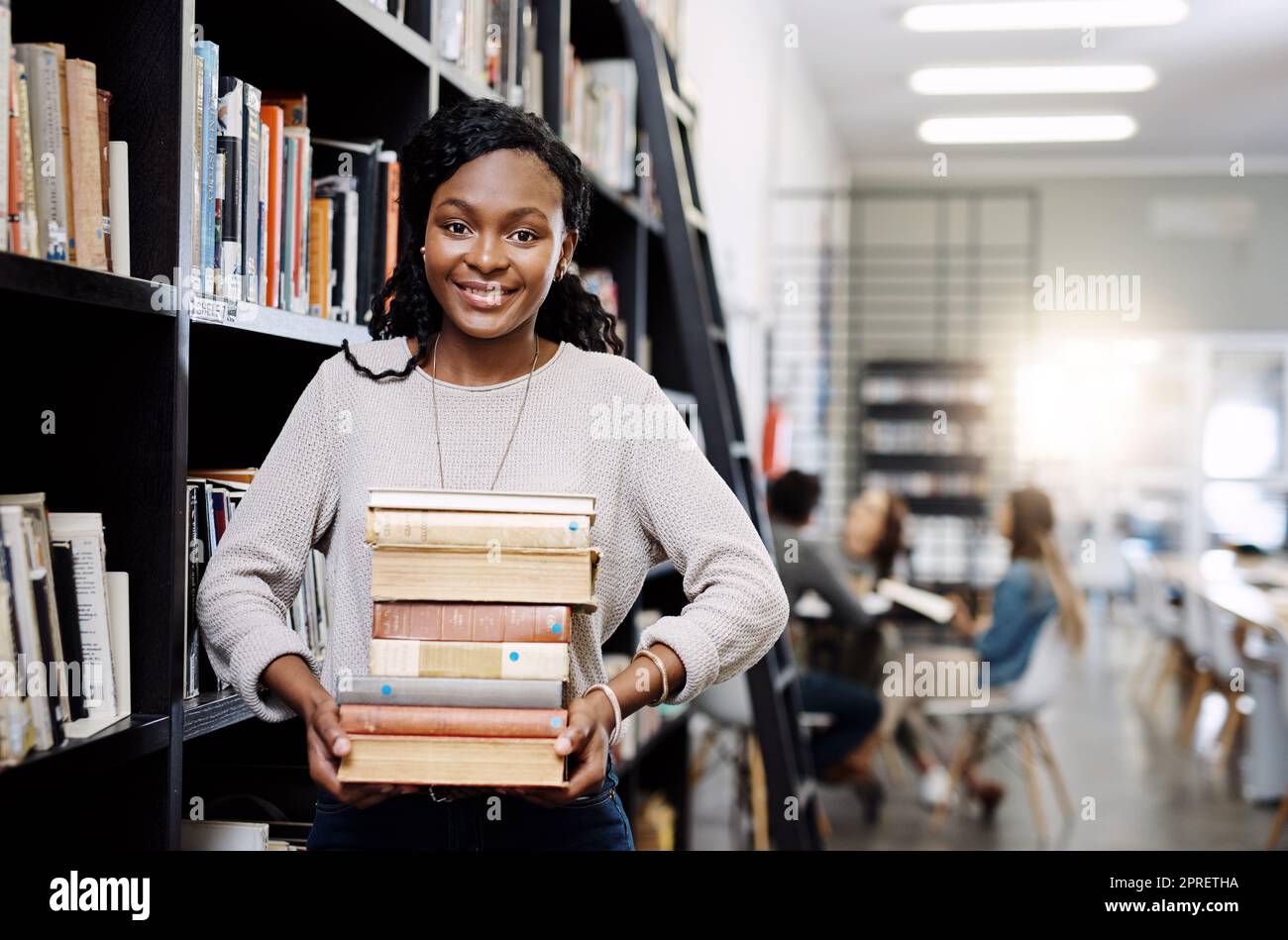 Viel zu lesen, viel zu lernen. Porträt einer glücklichen jungen Frau, die Bücher in einer Bibliothek am College trägt. Stockfoto
