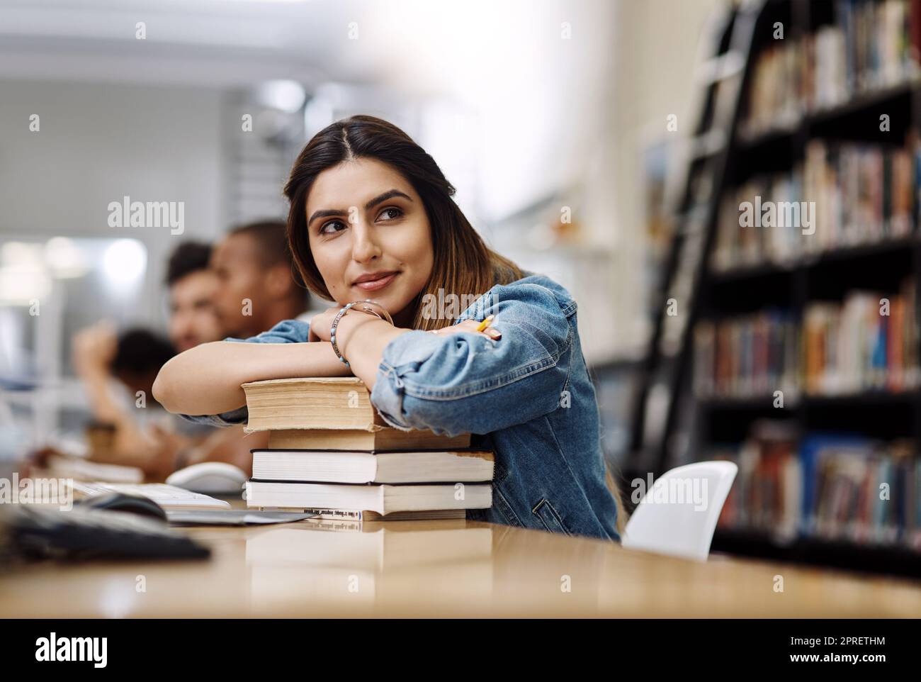 Shes hat die ganze Welt im Visier. Eine junge Frau, die sich in einer Universitätsbibliothek auf einem Bücherhaufen ausruhte und nachdenklich aussutete. Stockfoto