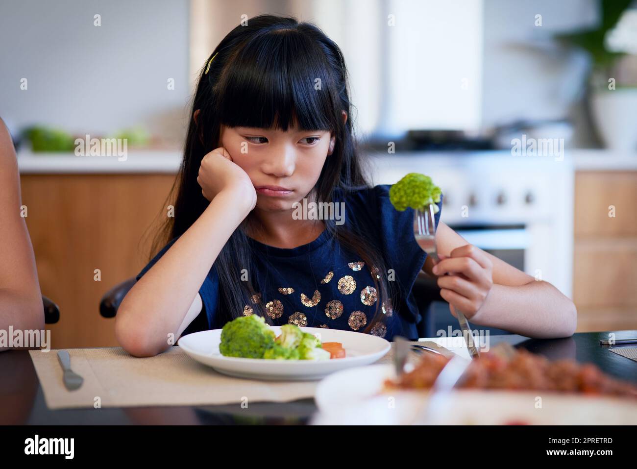 Warum werde ich wieder gefüttert. Ein kleines Mädchen weigert sich, ihren Brokkoli zu essen. Stockfoto