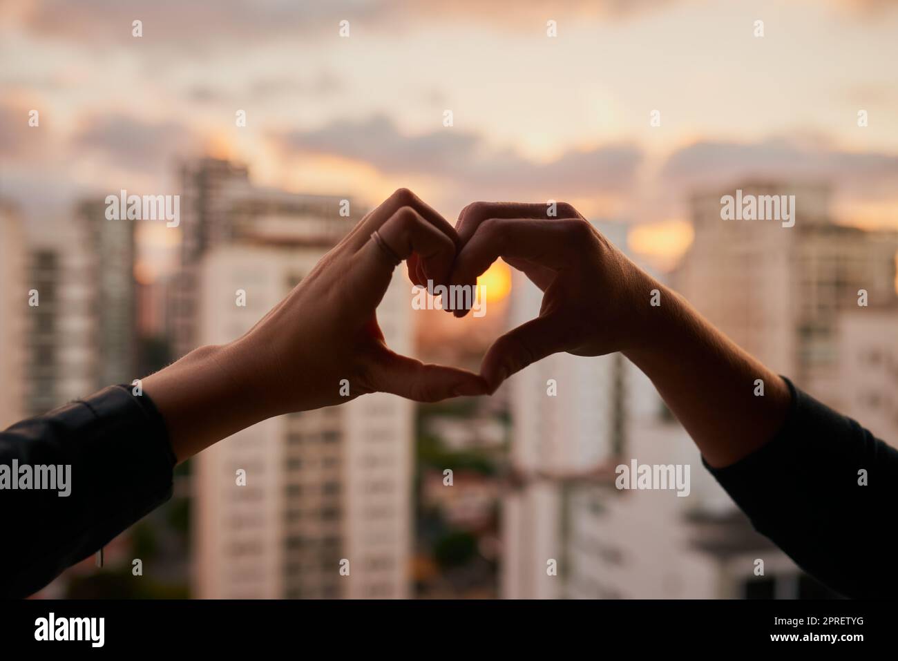 Wir lieben diese Stadt. Ein unverkennbares Paar, das mit den Händen vor einem Stadthintergrund eine Herzform macht. Stockfoto