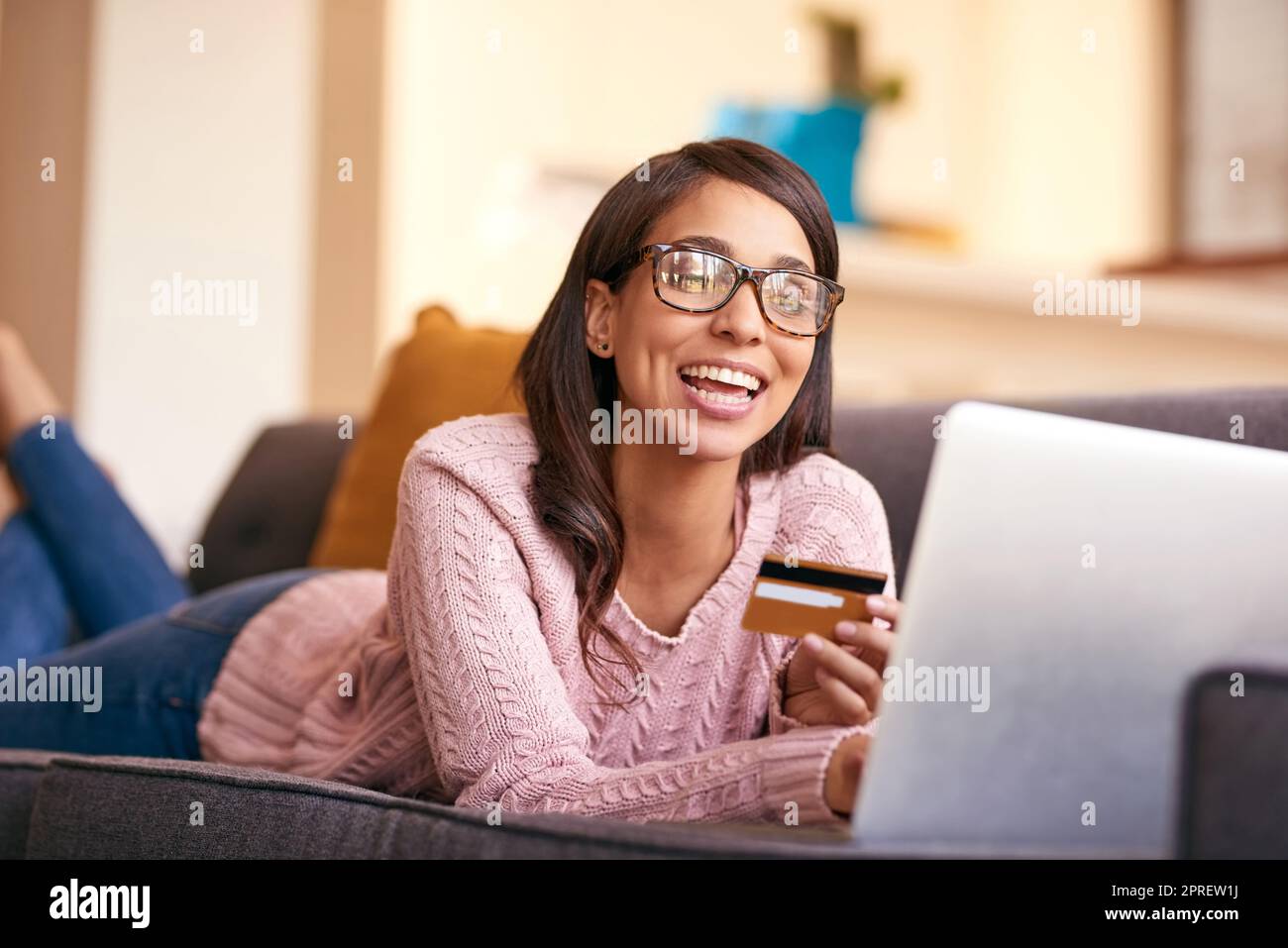 Eine attraktive junge Frau mit Laptop und Kreditkarte auf dem Sofa zu Hause. Stockfoto