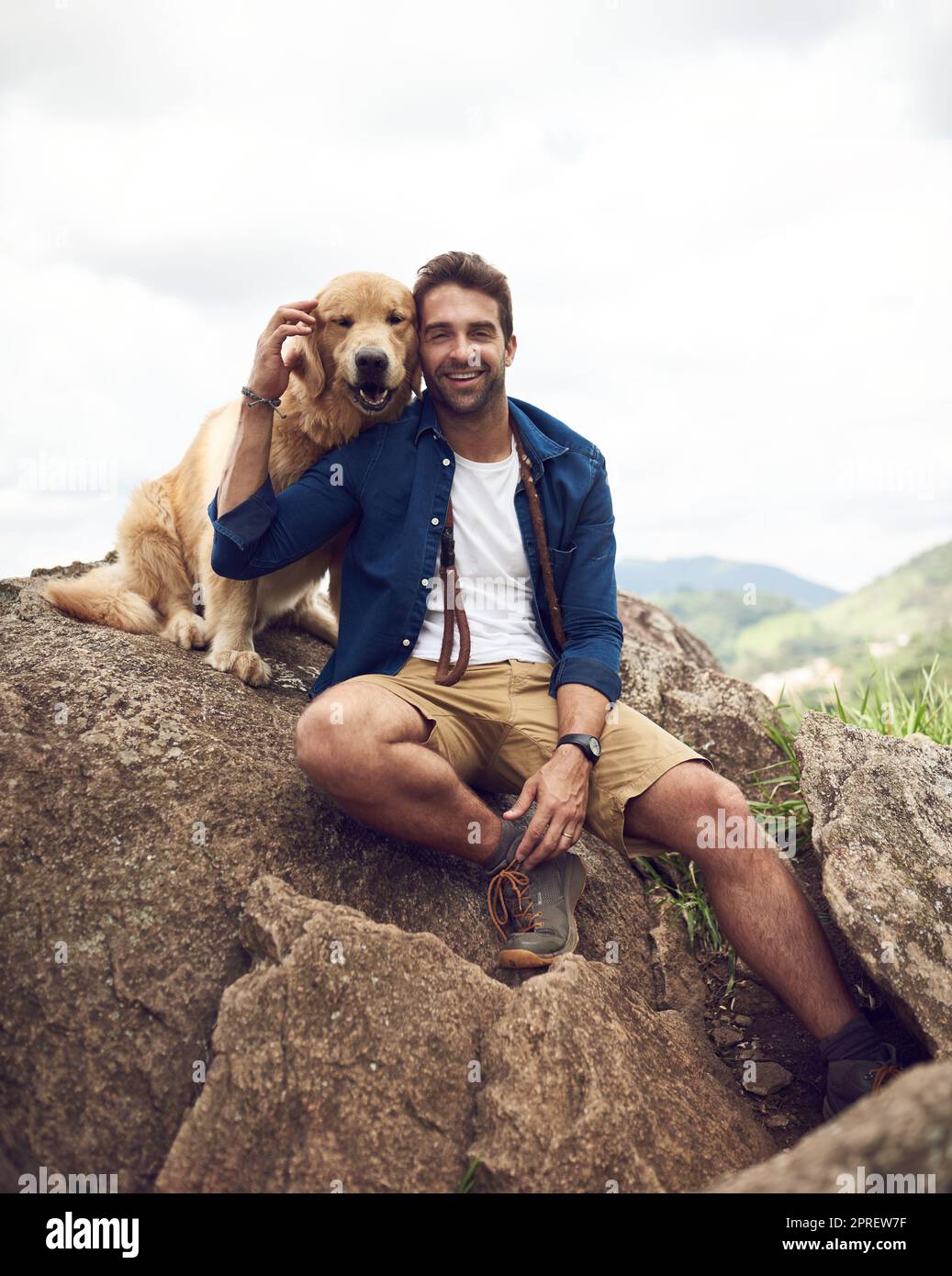 Mans bester Freund für das Leben. Ein hübscher junger Mann sitzt auf einem Felsen mit seinem goldenen Retriever nach einem Tag Wandern. Stockfoto