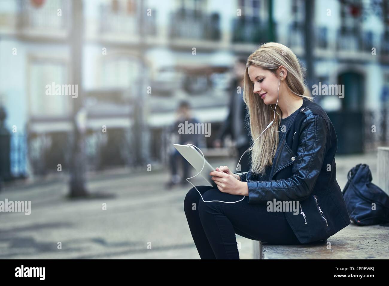 Denn Filmzeit passiert überall. Eine attraktive Frau, die in der Stadt ein digitales Tablet und Kopfhörer verwendet. Stockfoto