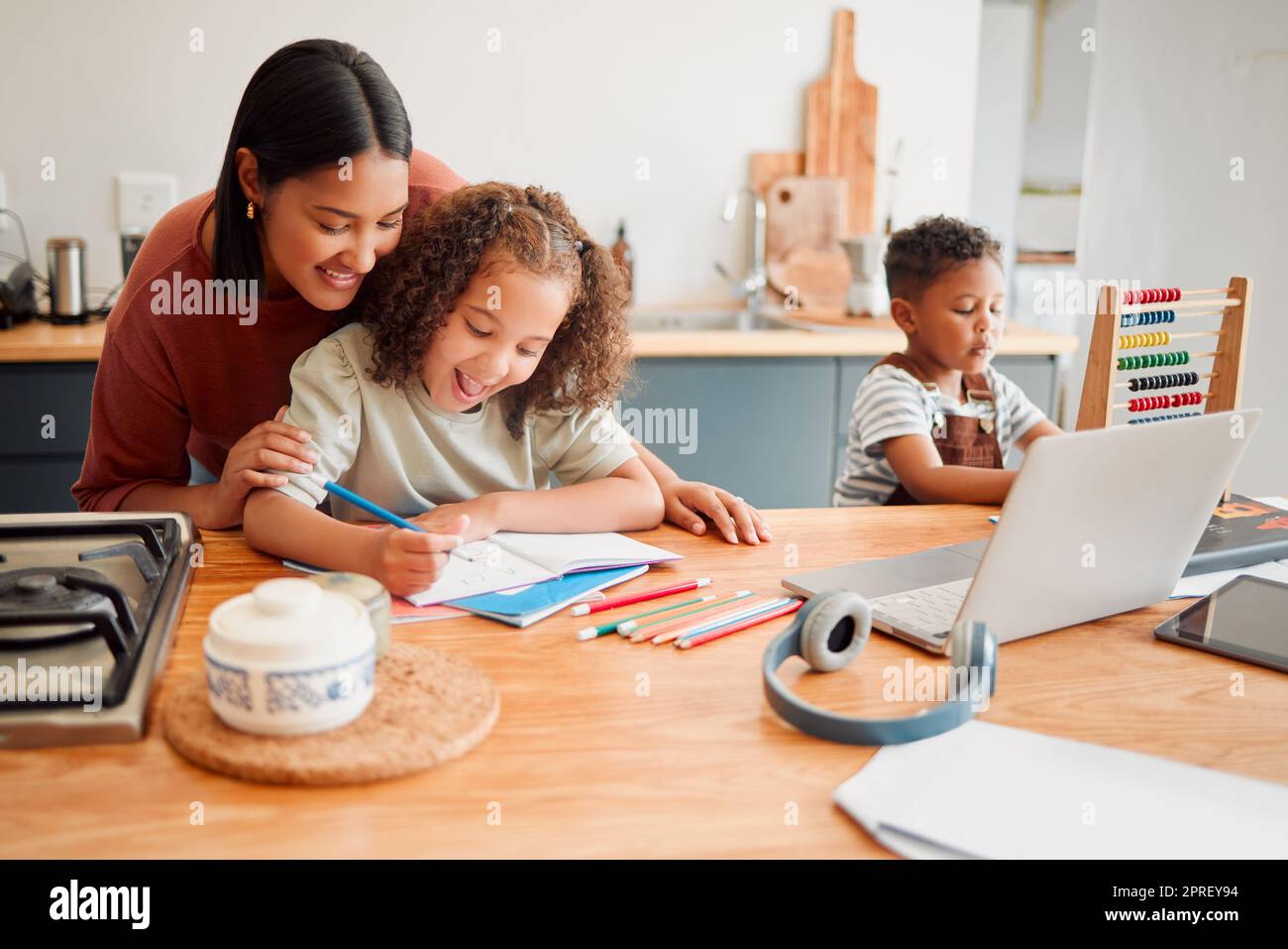Mutter und Kinder machen Hausaufgaben am Küchentisch, machen eine Bindung und genießen die Zeit mit der Familie zu Hause. Liebevolle Eltern helfen ihrer Tochter beim Zeichnen oder Zeichnen nach einem Online-Schulungsprogramm für Fernunterricht Stockfoto