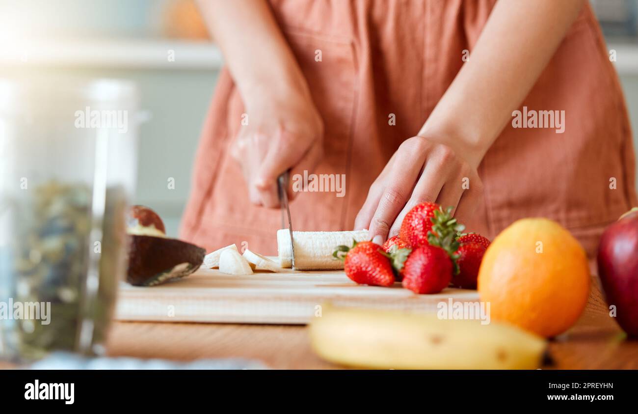 Gesunde Frau schneidet Obst, um einen Smoothie mit Nahrung für eine Bio-Diät zu Hause zu machen. Nahaufnahme weißer weiblicher Hände, die frische Produkte für ein Gesundheitsgetränk in einer Küche hacken. Stockfoto